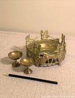 Photo showing three brass items arranged on a carpeted surface, including one large ornate bowl and two smaller chalice-shaped bowls, with a pencil included for scale.