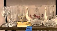 Shelf of assorted clear glassware, crystal glasses, glass bowls, and ceramic swan figurines.