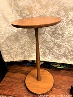 Full view of the round vintage wooden table showing top, pedestal leg, and base against a floral curtain background.