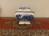 Front view of the vintage ceramic soup tureen with a blue and white pastoral landscape design and matching lid.