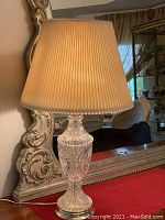 Full view of the vintage crystal lamp with pleated shade on a table with an ornate mirror in the background.