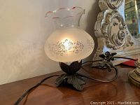 Side angle showing the lamp lit with frosted glass shade and cherub on metal arm base