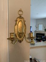Front view of brass wall sconce showing backplate and two curved arms with candle cups.