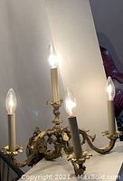 Close-up image showing four illuminated candle-style bulbs mounted on ornate brass arms with detailed Victorian design.