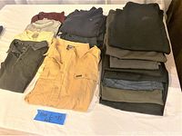 Overview of the men's clothing lot size large showing shirts, jackets, sweaters, and pants folded on a table.