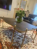 Full view of the antique coffee table with a dark brown leather top and gold metal legs, placed on a patterned rug in a living room setting.
