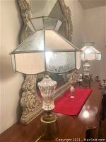 Pair of vintage table lamps with brass bases, faceted crystal midsections, and stained glass multi-paneled shades, seen on wooden surface in front of a large decorative mirror.