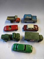 Seven die-cast vehicles arranged on white surface showing top and side views of each vehicle with visible wear and paint chipping.