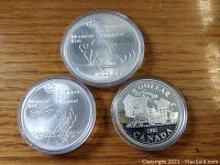 Three coins in capsules showing reverse designs: hockey player, swimmer, locomotive