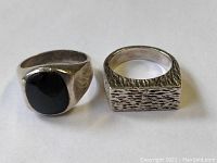 Two sterling silver rings on white background; one with black cabochon stone, one with textured square band.