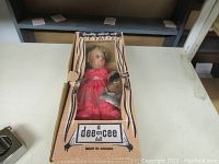 Full view of vintage Dee An Cee doll in original box showing pink dress and visible face with platinum hair.