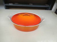 Full image of the vintage Le Creuset orange enamel casserole dish with lid showing the oval shape and handles.