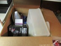 Photo of a cardboard box containing black Eliminator battery charger box, plastic bottle of clear liquid, and a large translucent plastic storage container