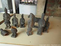 Photo of all 8 resin Terracotta Warrior statues arranged on a surface showing various conditions including one damaged statue missing head and torso and one horse statue