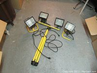 Photo showing the four halogen flood lights with yellow tubular bases alongside the yellow tripod stand with cords laying on floor