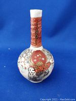 Front view of ceramic vase showing the bulbous body, narrow neck, and hand-painted Japanese-style faces and floral decoration with gold accents.