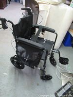 Side view of the black folding wheelchair showing armrests, footrests, and fabric seat.