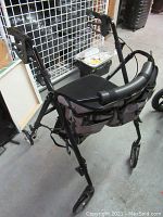 Side view of walker showing four small wheels, padded seat, camouflage fabric storage pouch and backrest, hand brakes on handles.