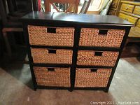 Photo of front view of black wood framed storage unit with six rattan drawers arranged in two columns and three rows.
