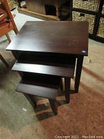 Three nested wooden tables with dark brown finish showing full lot.