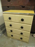 Full view of a retro style yellow veneered 4-drawer unit with black round knobs and visible wear.