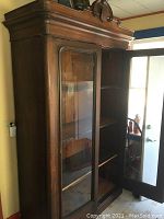 Front angle view showing the mahogany wardrobe with two glass panel doors open to shelving inside. The craftsmanship details and finish are visible.