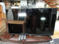 Samsung 44-inch TV on stand with two remotes in front, screen off showing reflection.
