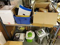 Photo of shelving showing multiple bins with assorted household items including knife block, cameras, cooking and cleaning items.