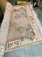 Rolled wool carpet showing floral design with reddish, cream, and blue flowers and leafy vines on beige background.