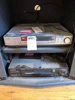 Two media players stacked on a shelf: RCA DVD player on top and Panasonic VHS player below, both dusty and untested