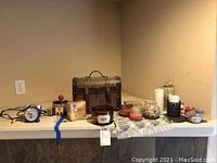 Photo showing various home decor items on a table, including a small chest, multiple candles, a blue vintage style twin bell alarm clock, and other decorative pieces.