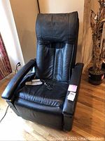 Front view of black electrical massage chair with remote on seat, showing padded headrest and armrests.