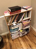 Front view of a white bookcase filled with books and papers, showing visible disrepair and clutter.