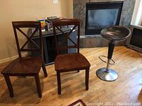 Two dark brown wooden chairs with cross-back design on wood floor near fireplace