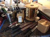 Five kitchen knives with black handles, wooden knife block, wooden rotary spice rack with spice containers, and additional wooden containers on countertop