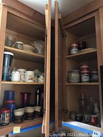 Open cabinet showing tea cups, mugs, saucers, plates and glassware inside wooden shelves.