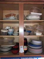 Wide view of cabinet shelves with multiple plastic storage containers stacked on top with matching lids, ceramic bowls with various sizes and patterns on the left middle shelf, and stacks of plates and bowls on bottom shelf.