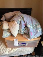Memory foam pillow, comforter, bedsheets on top of beige plastic storage drawer.