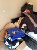 Large plush teddy bear on floor near bed surrounded by bags containing clothes