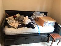 Twin size painted wood daybed frame shown with mattress and miscellaneous items on top. Shows dark finish and decorative drawer-front panels below mattress support slats that are not functional drawers.