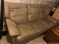 Front view of the tan leather couch showing three attached cushions and wear on the seats.