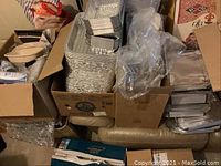 Photo showing several boxes containing stacks of aluminum pans and other disposable catering supplies.