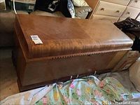 Full front side view showing waterfall design on front panel, veneer damage on lower right, curved top lid, and carved trim detail beneath lid.