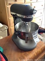 Full view of gray KitchenAid Professional 5 Plus mixer on table with stainless steel bowl and balloon whisk attachment.