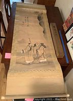 Full length view of the antique Japanese scroll unrolled on table showing figures, calligraphy, and fabric border.