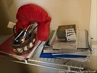 Wide view showing red travel neck pillow, woven basket with pens, stack of school notebooks, and music box resting on surface.