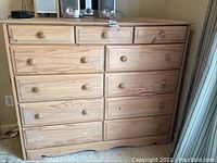 Front view of solid wood chest of drawers with three small upper drawers and eight larger drawers beneath. Knobs on some drawers are missing, wood grain is visible, some surface marks and scratches.