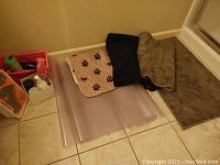 Photo showing three bathroom rugs and clear plastic runner mat on tile floor with some cleaning products and totes visible at left