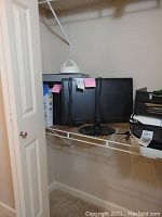 Two computer monitors on a shelf beside a computer tower and other miscellaneous items.