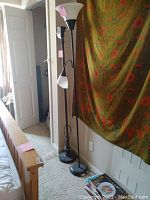 Two floor lamps and one table lamp near a bed and window. One floor lamp has a pink and white glass shade, the other floor lamp has no shade. The table lamp has a white shade.